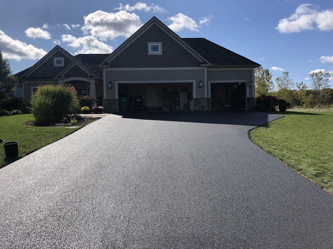 Finished asphalt driveway in front of a ranch house with a three car garage, asphalt paving