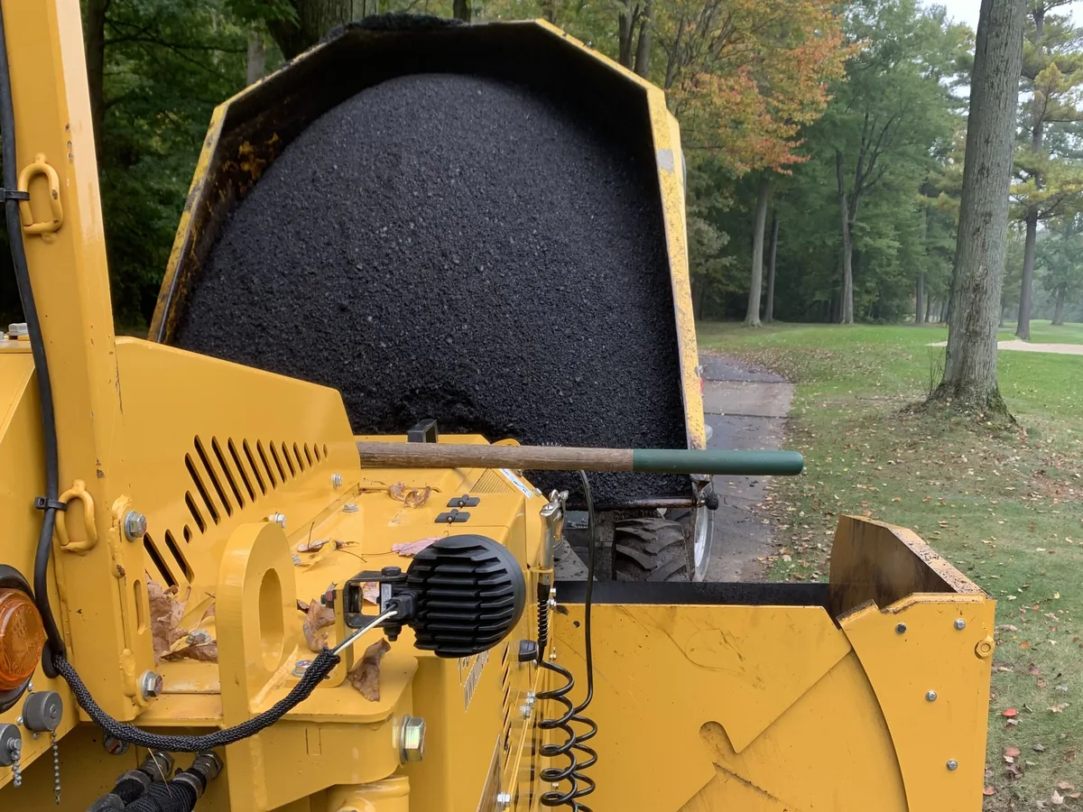 Asphalt paver hopper loaded with hot mix beside a fresh mat on a paved path, asphalt paving
