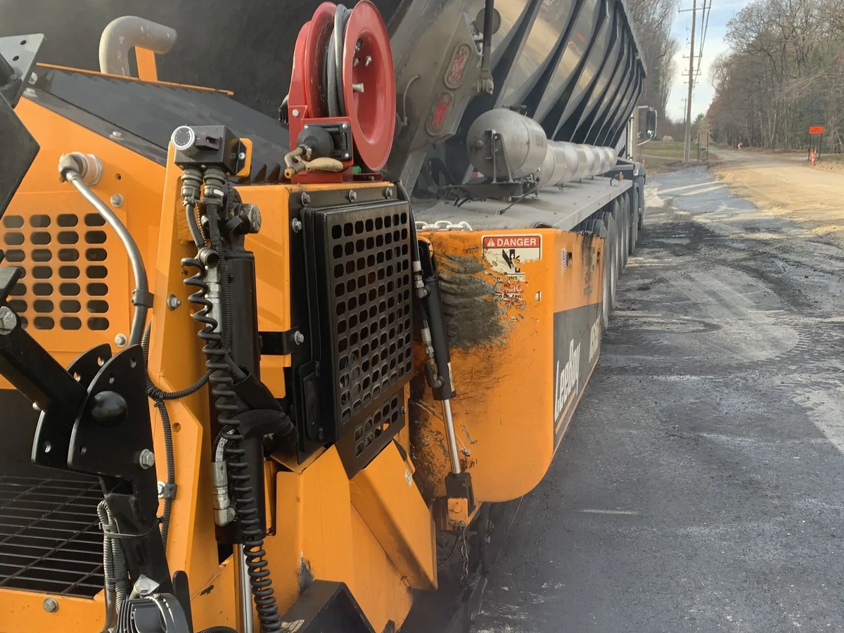 Asphalt paver laying a new mat along a road behind a dump truck, asphalt paving