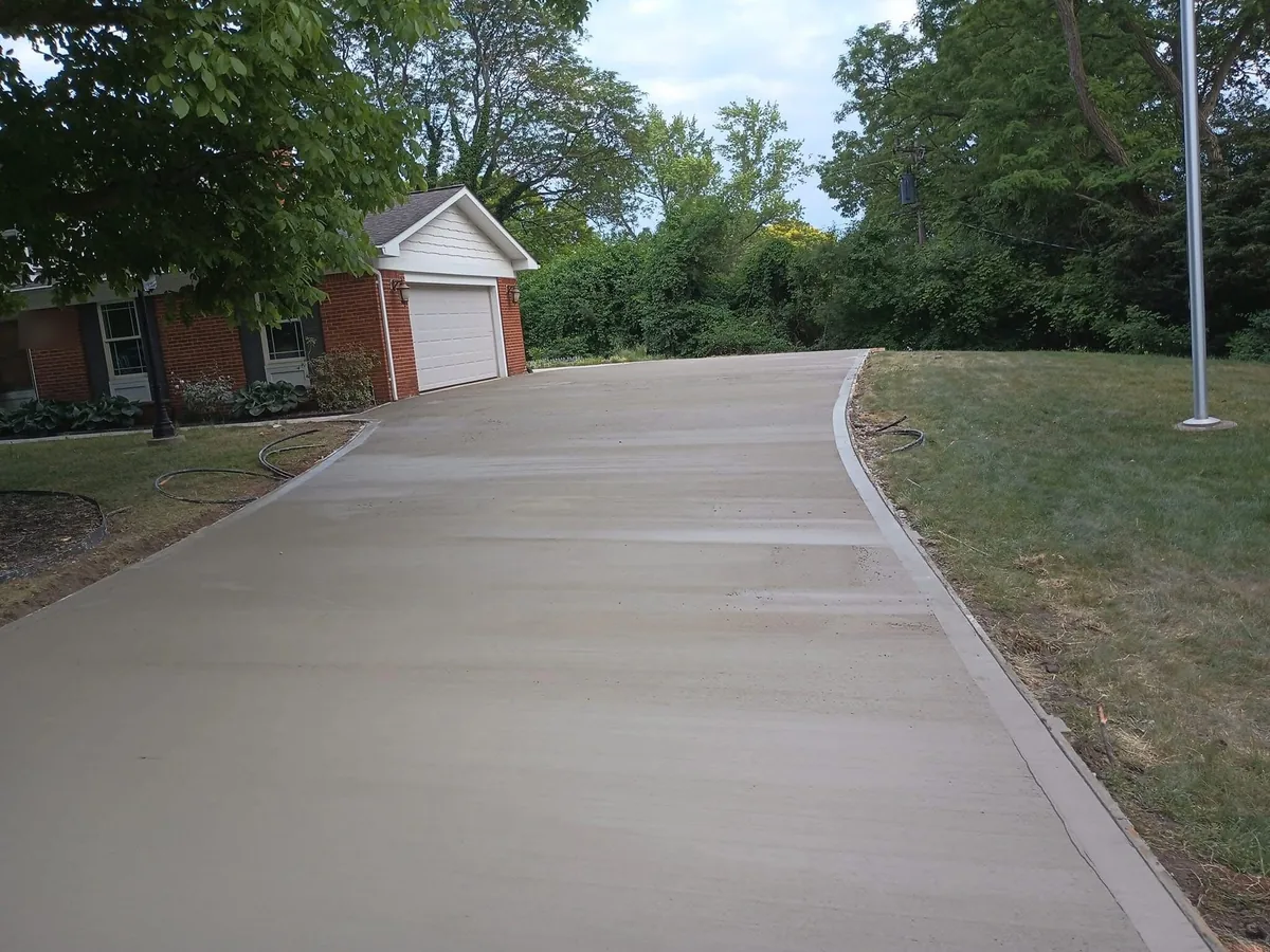New concrete driveway with control joints curving to the garage of a brick ranch house, concrete driveways