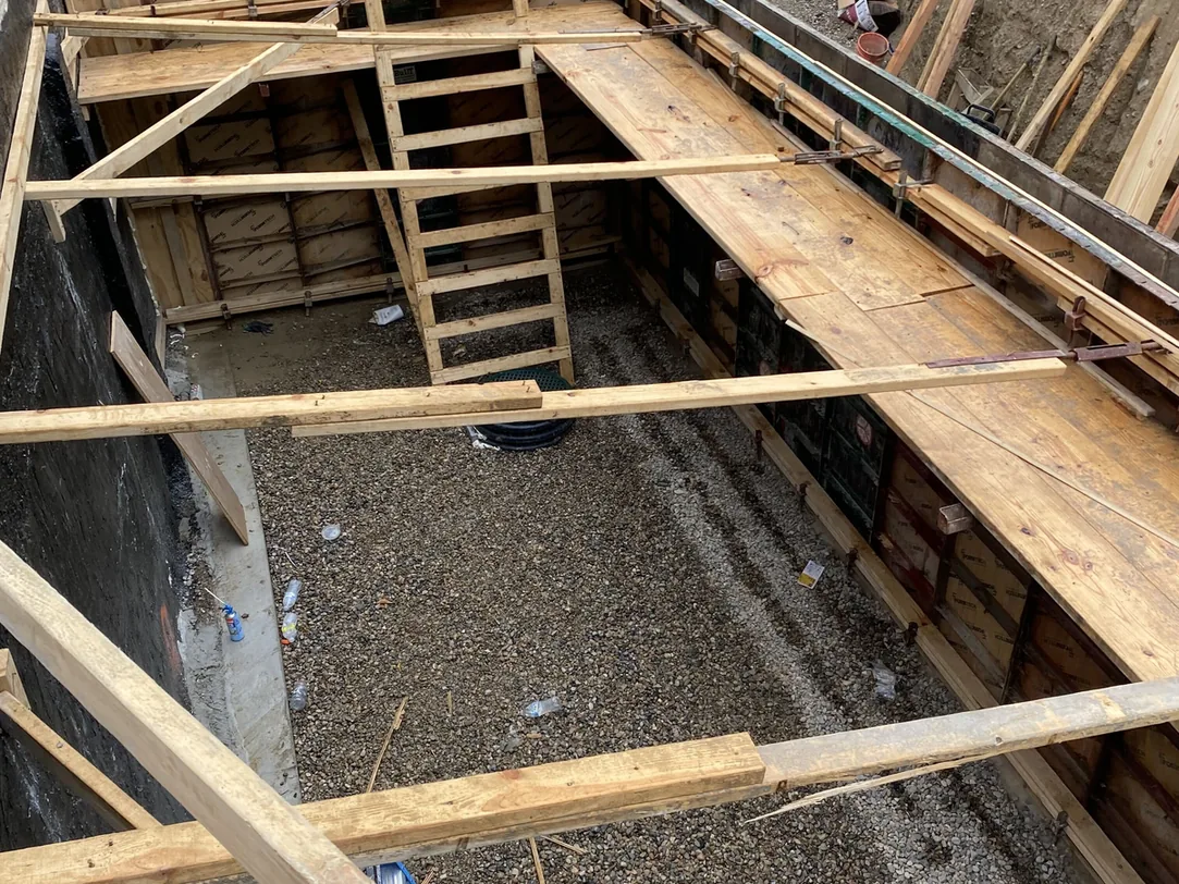 Wood forms set for footings and a foundation wall in a dug out addition with a ladder, concrete foundations and footings