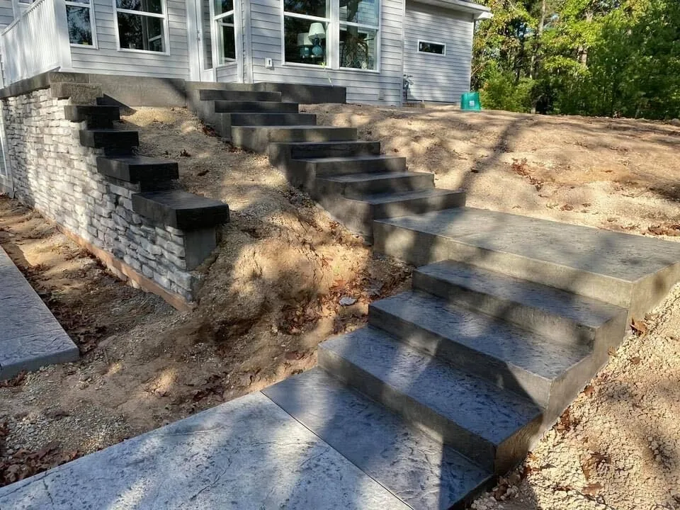 Concrete steps cascading down a slope beside a stone retaining wall, concrete steps