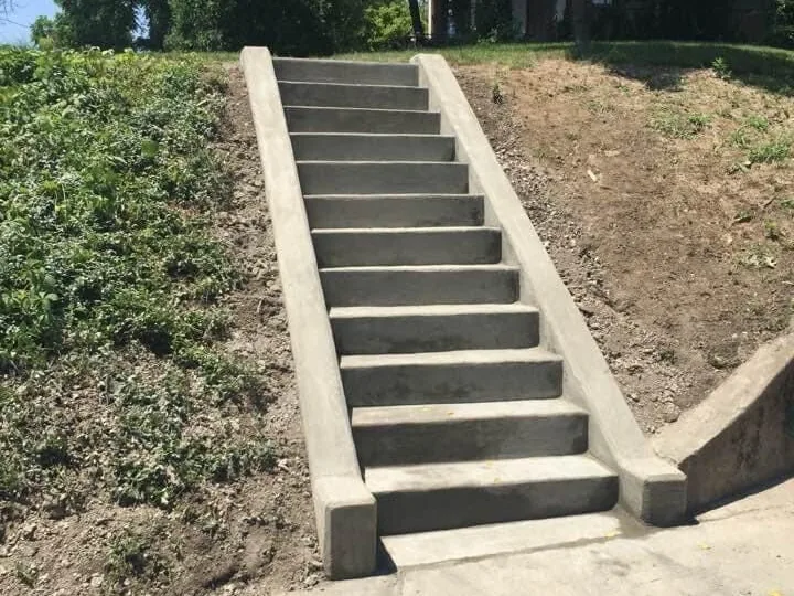 Straight concrete stair with side walls climbing a grassy bank, concrete steps and stairs
