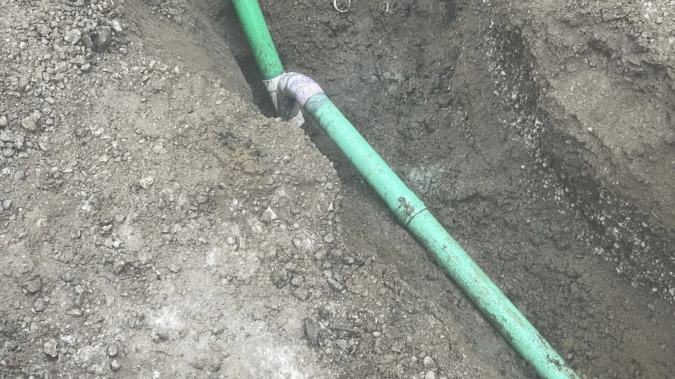 New green PVC sewer line with a wye fitting bedded in a gravel trench, sewer line work
