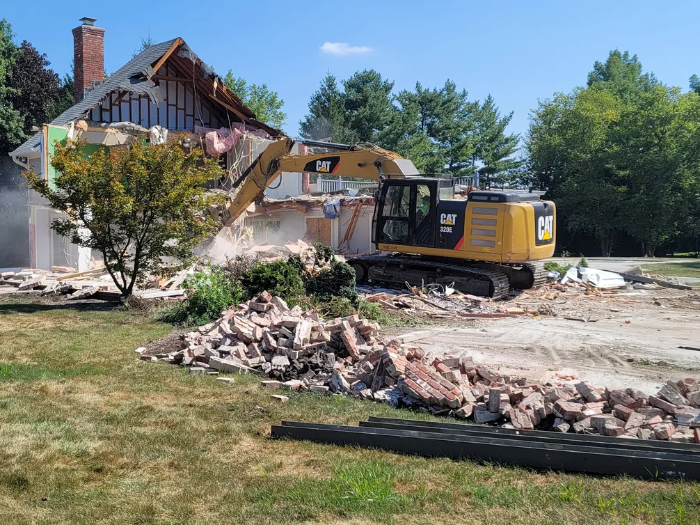 Excavator tearing down a two story house with a brick chimney, brick piled on the lawn in front, house demolition