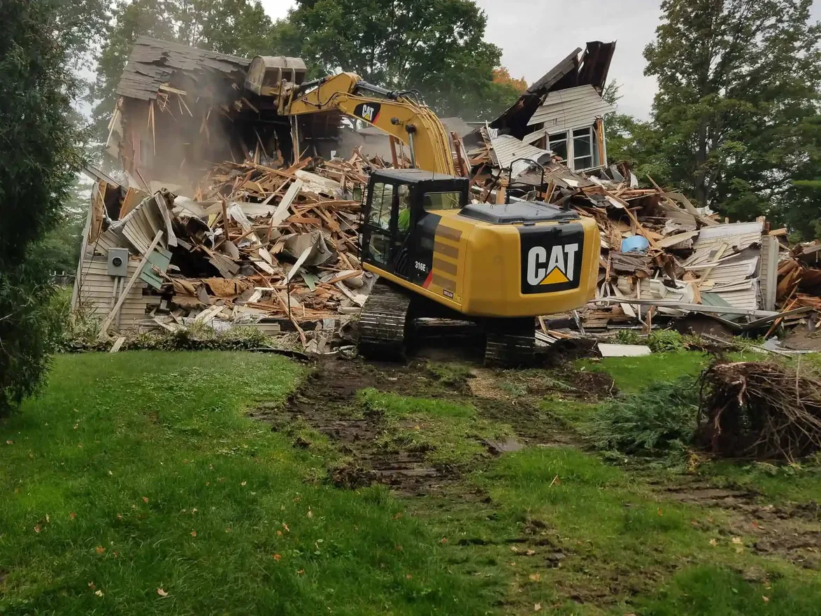 Excavator pulling down the last walls of a house into a pile of debris on a wooded residential lot, residential demolition