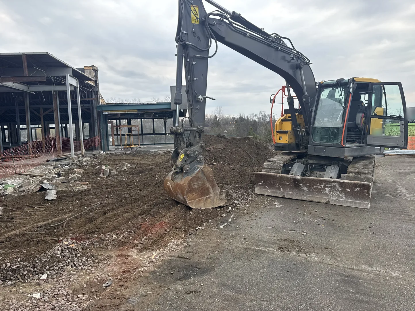 Excavator with its bucket down on a cleared commercial site beside a building under renovation, excavation and site work