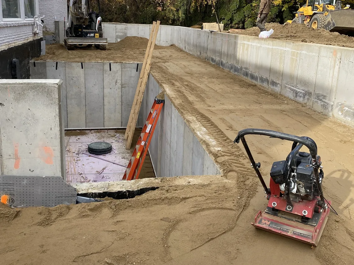 Plate compactor in a foundation excavation beside new walls, excavation and site work
