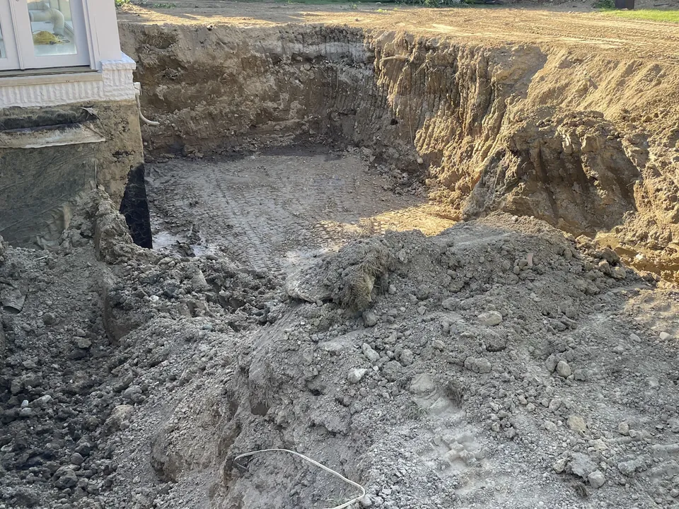 Large excavation dug beside a white house with spoil and a level bottom, excavation and site work