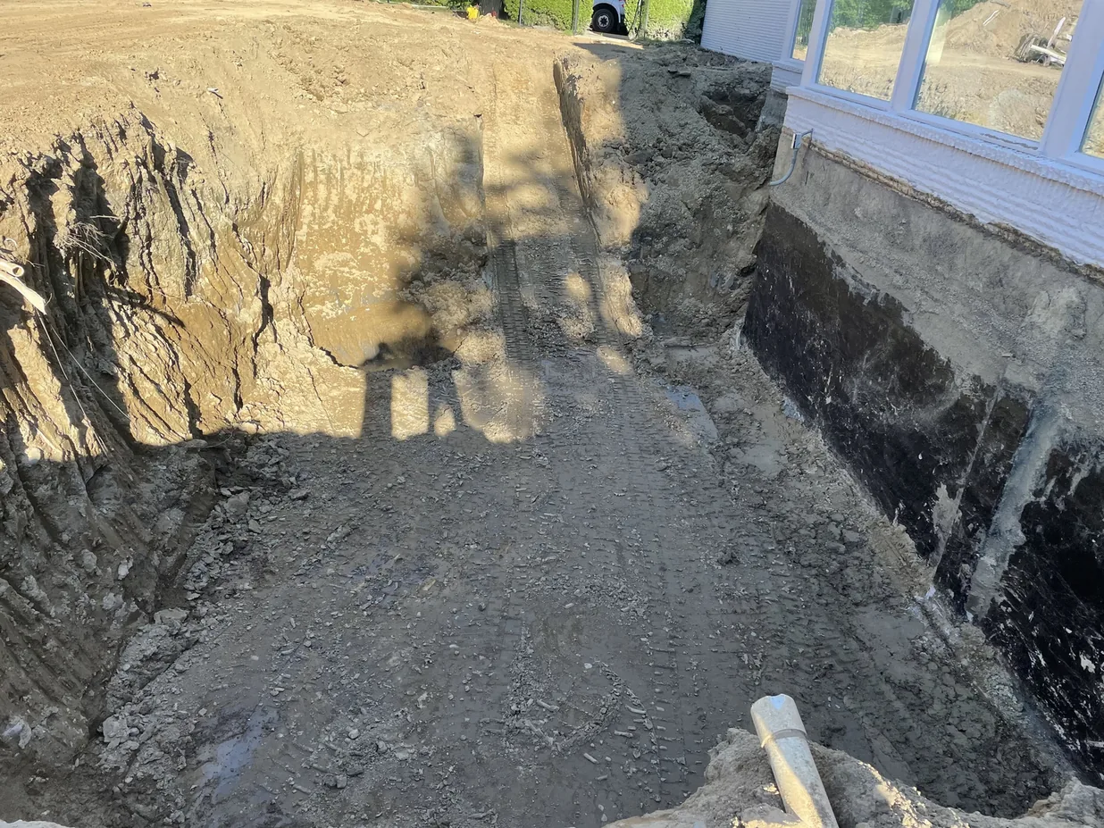 Excavation along a foundation wall coated with black waterproofing, foundation waterproofing