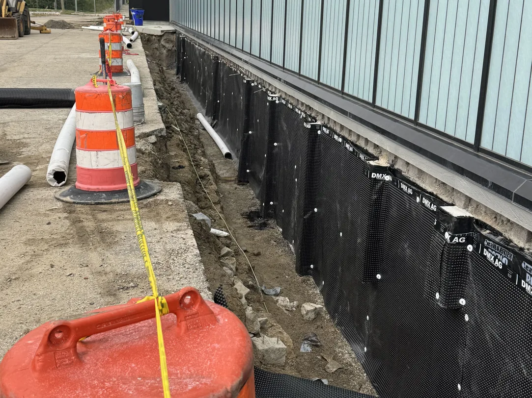 Footing drain pipe and waterproofing membrane in a trench along a commercial building, foundation waterproofing