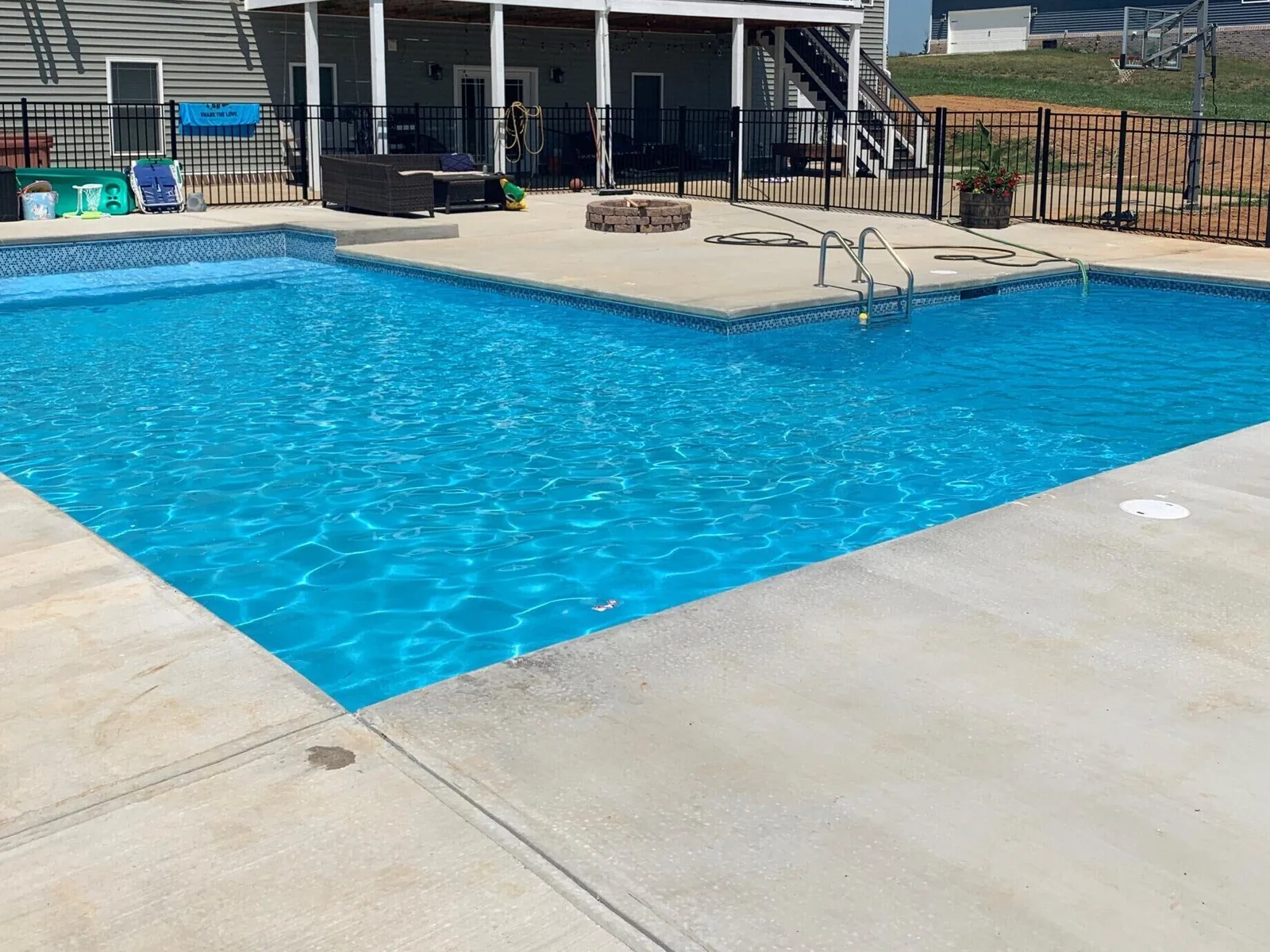 Finished inground pool with a broom finish concrete deck, a fire pit and a black aluminum fence, inground pools