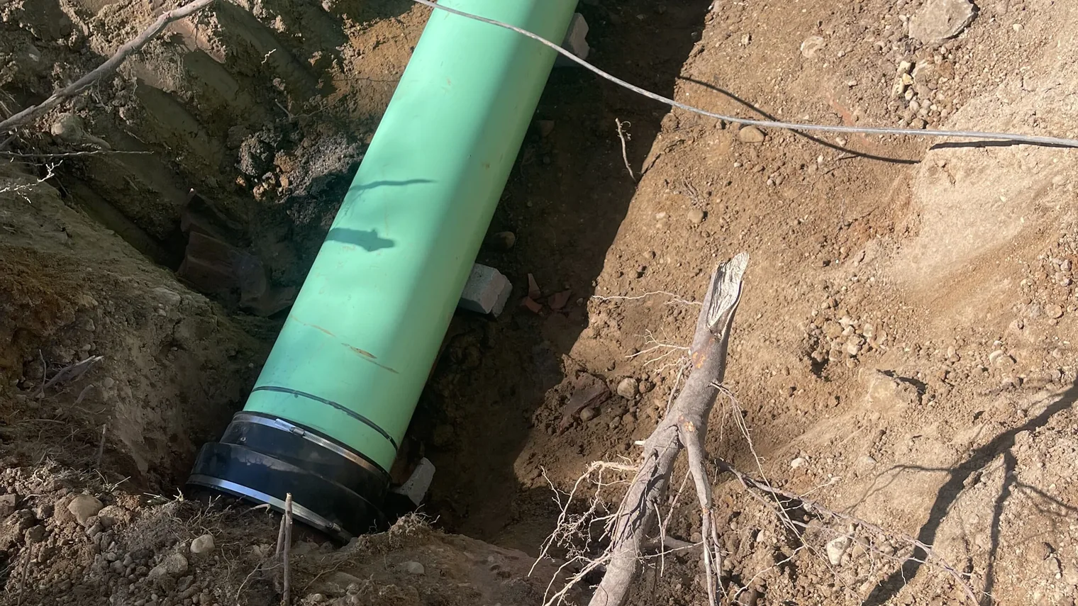 Large green PVC pipe with a gasketed coupling laid in a rooty trench, underground pipe work