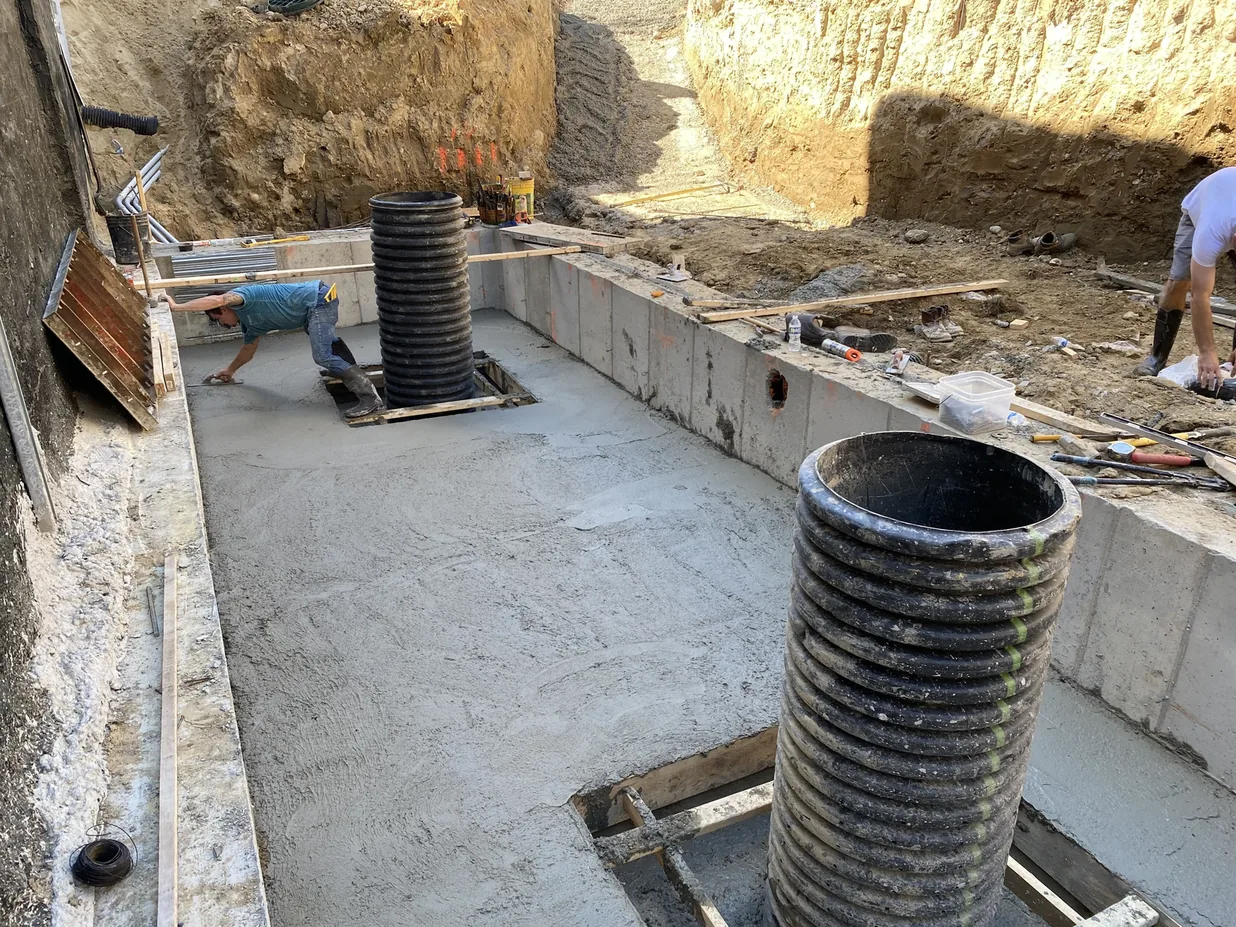 Crew finishing the floor of a poured concrete vault with black risers on a commercial site, construction project management