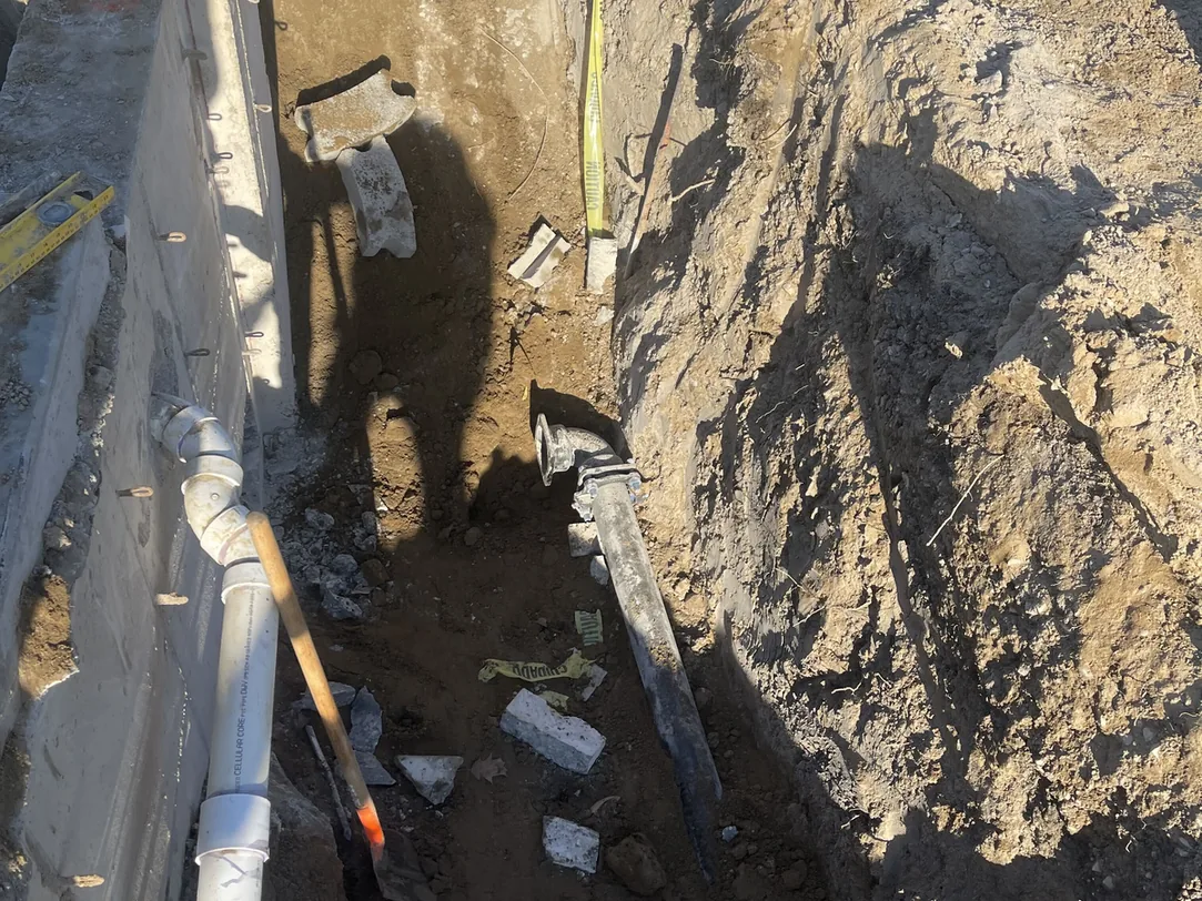 Utility trench with PVC lines along a precast wall behind caution tape, construction project management