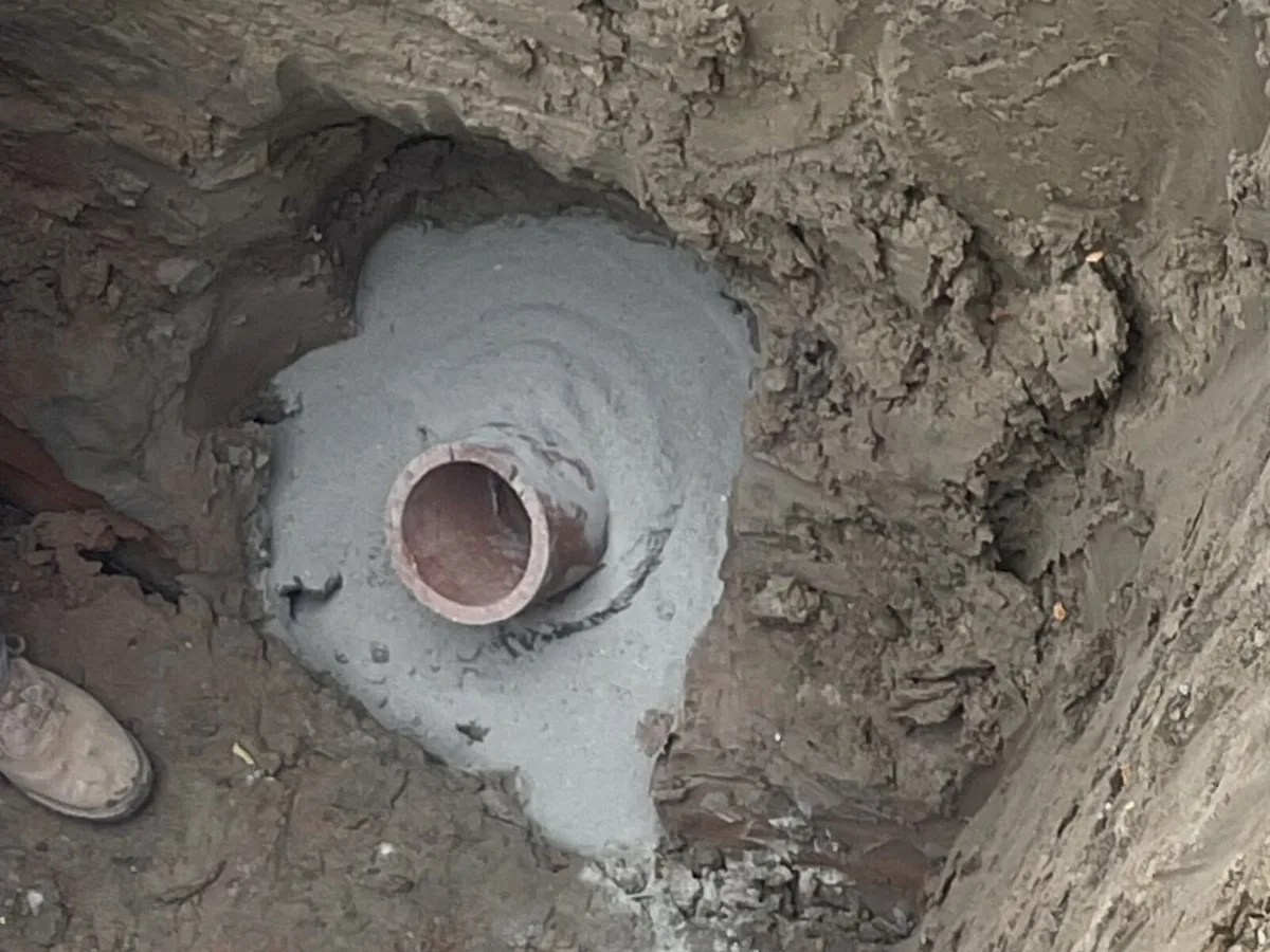Old clay pipe connection set in a fresh concrete collar at the bottom of a dug pit, septic system repair