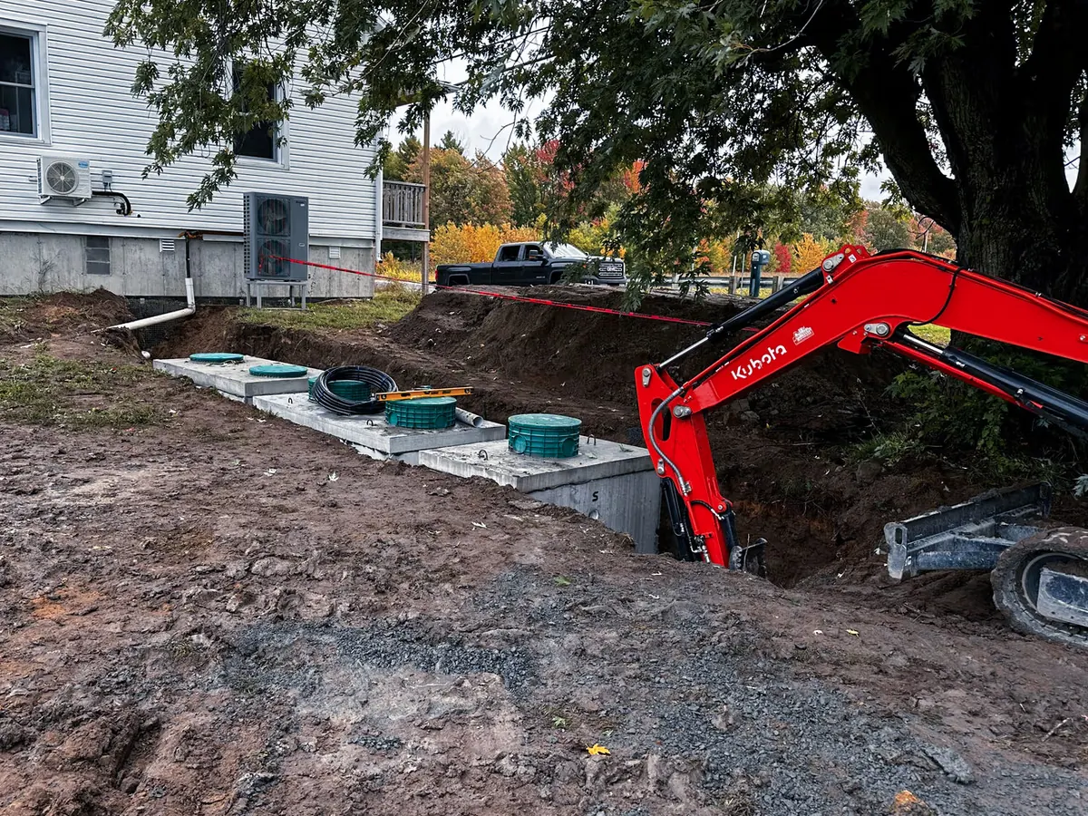 New concrete septic tanks with green riser lids set in a trench beside a house as a mini excavator works, septic system repair and tank replacement