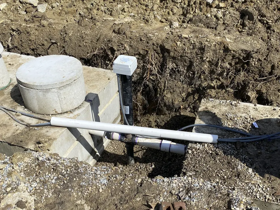 Concrete septic tank with a riser, a pump alarm post and new PVC pipes in a fresh dig, septic system repair