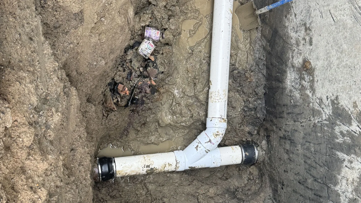 New white PVC sewer tee joined to the old line in a dug trench, site and underground utility work