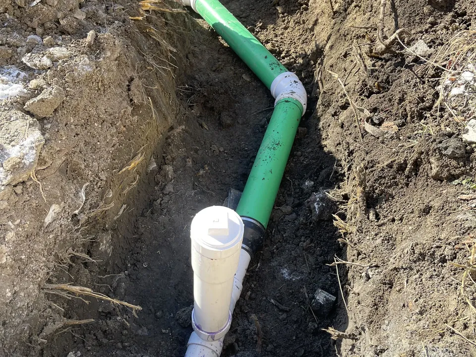 New green PVC sewer line with a white cleanout tee and wye in a dug trench, sewer line replacement