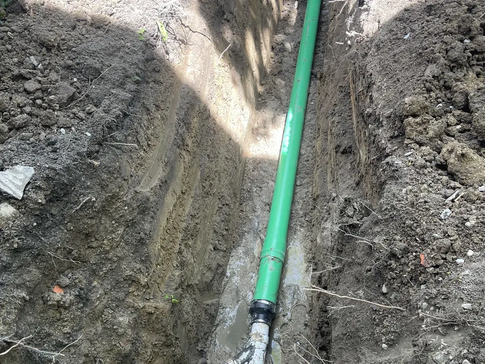 Long narrow trench with a new green PVC sewer pipe joined to the old line, sewer line replacement
