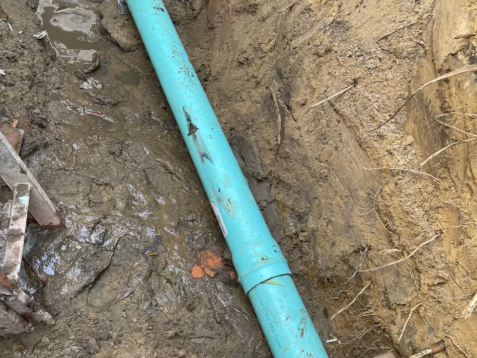 New green PVC sewer pipe joined to the old line with a rubber coupling in a muddy trench, sewer line repair
