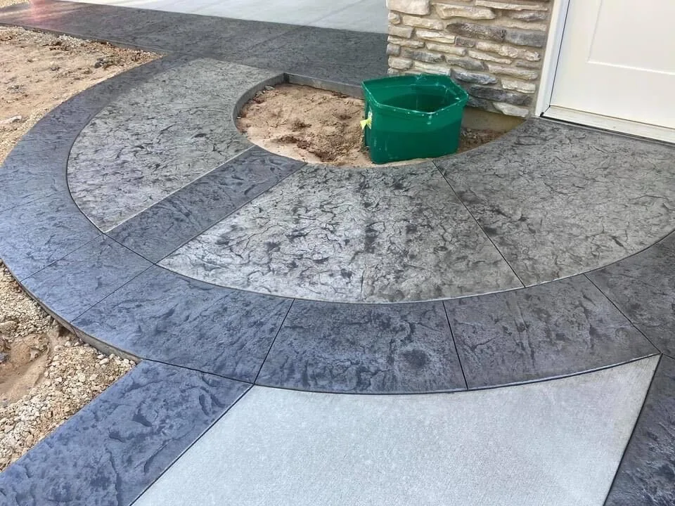 Stamped concrete curved walk with a dark border around a planter by a garage, stamped concrete