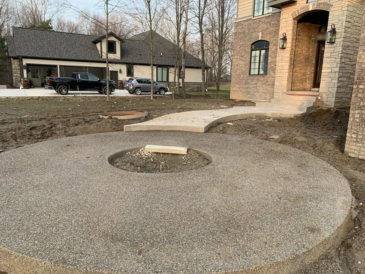 Exposed aggregate concrete circle with a fire ring opening and a walk at a stone and brick house, stamped concrete and exposed aggregate