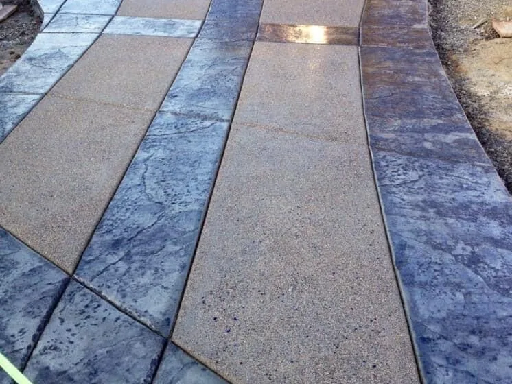 Curving walkway with stamped concrete bands and exposed aggregate panels leading to a garage, stamped concrete