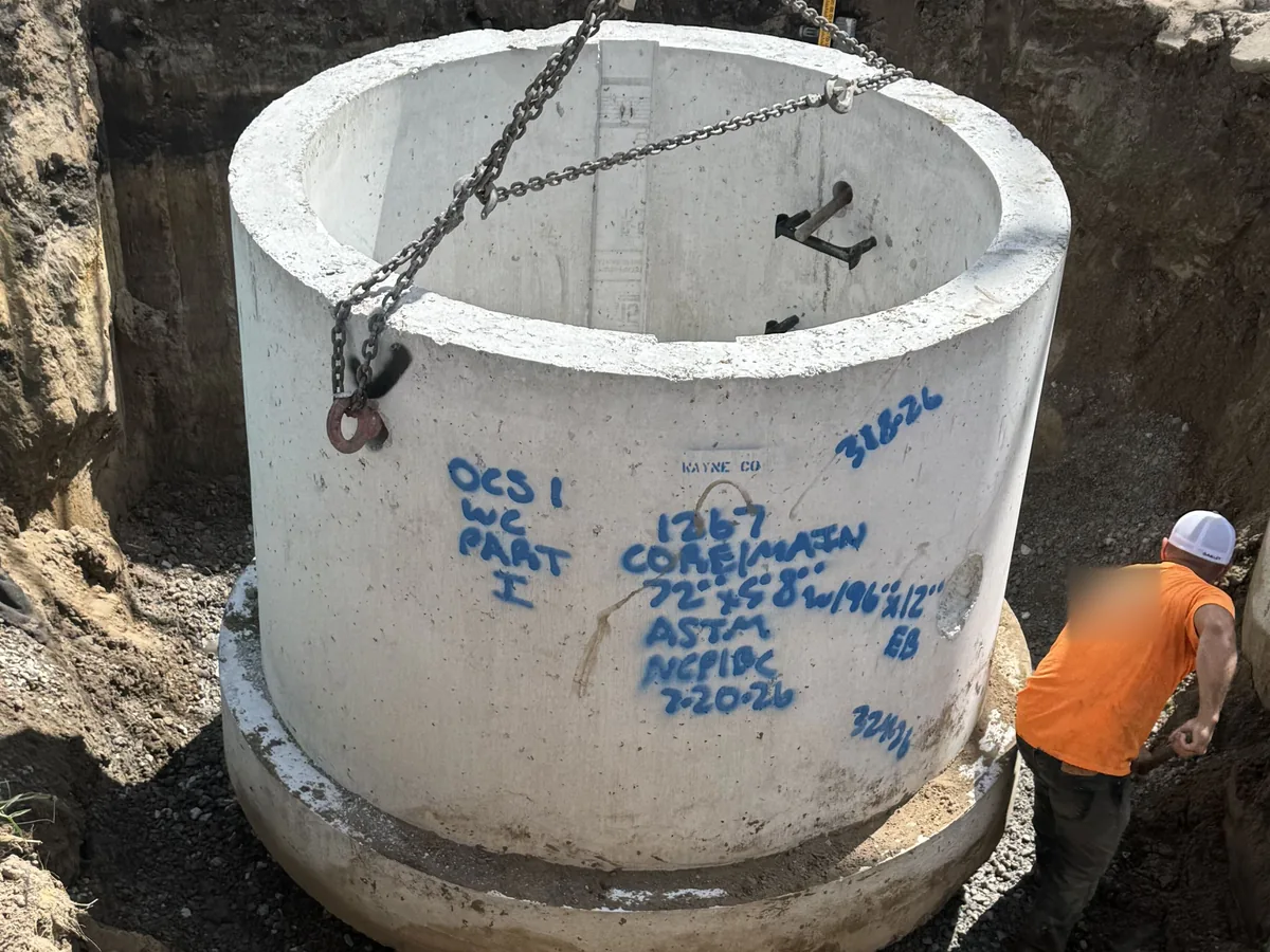 Large precast concrete manhole section lowered on chains into an excavation, storm drainage