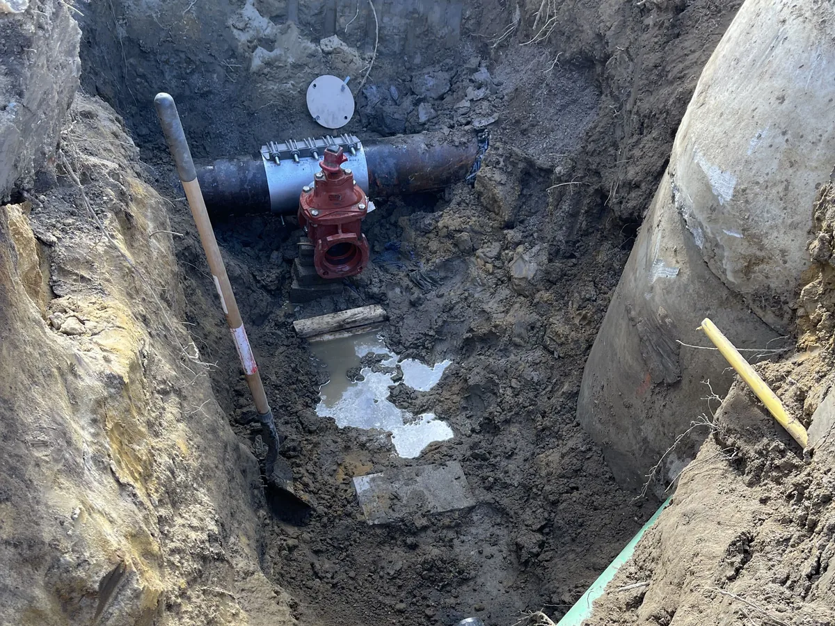 Red gate valve and a stainless repair clamp on a water main in an open trench, water main installation and repair
