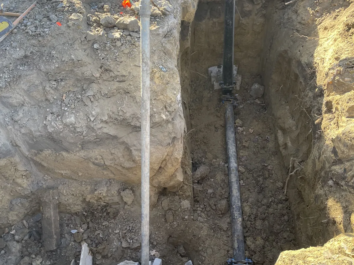 Water main pipe on blocks with a valve box riser in an excavated pit, water main installation